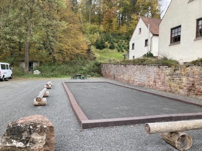 Eingefasste Boulebahn am Rand eines Parkplatzes